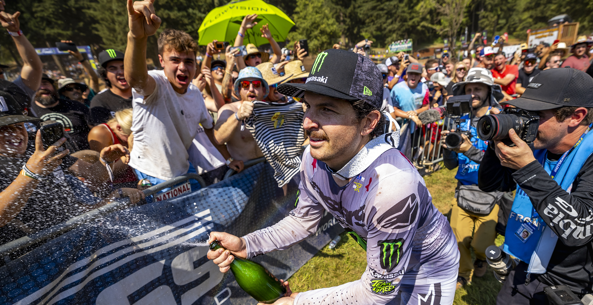 Jason Anderson wearing Alpinestars mx apparel celebrating with a bottle of champagne in front of a crowd after a motocross race.