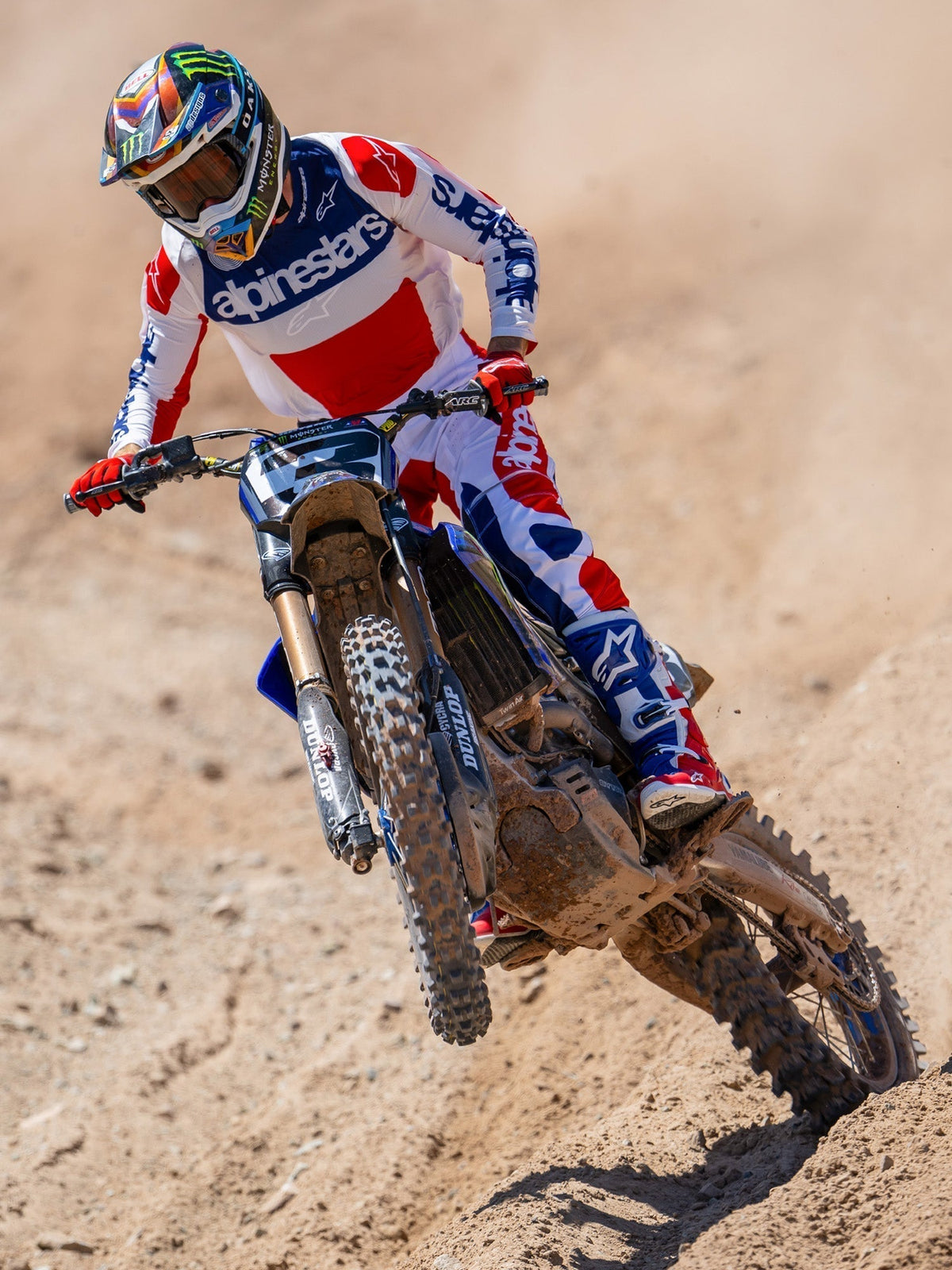 Motocross rider in action on a dirt track, wearing the Limited Edition Techstar Fortitude Jersey in Bright Red White and Blue, coordinated with matching racing pants and boots, featuring bold Alpinestars branding, professional off-road racing apparel