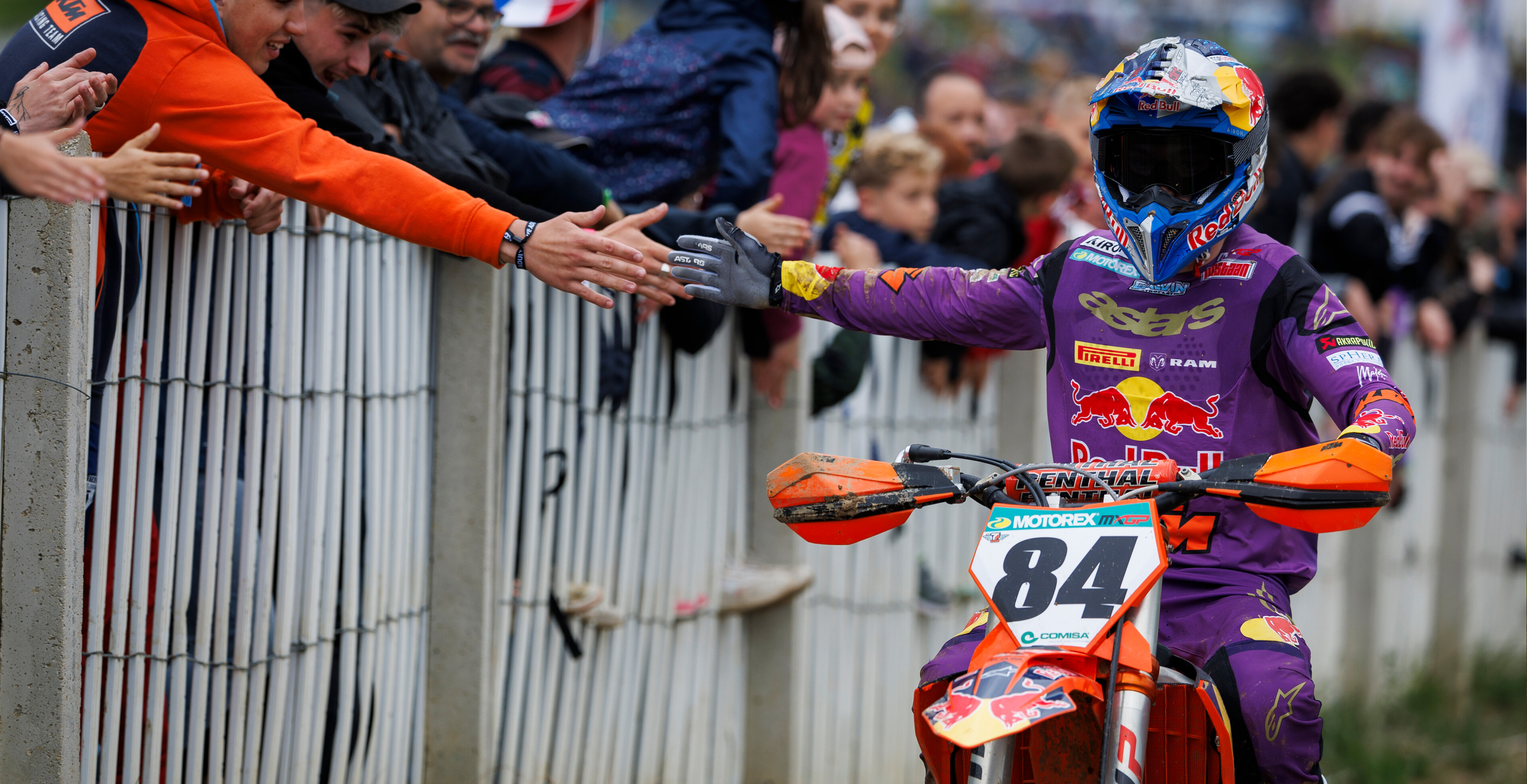 Motocross rider in purple Alpinestars gear with number 84 on a KTM bike, surrounded by spectators.