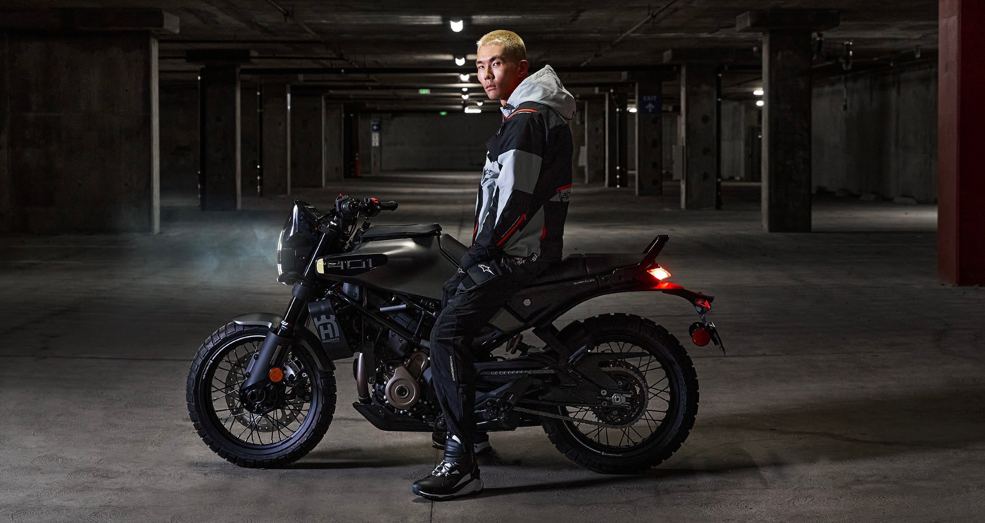 Alpinestars Mogress Air Jacket, Blue Almond urban motorcycle jacket with hood, worn by a man on a bike in a garage.