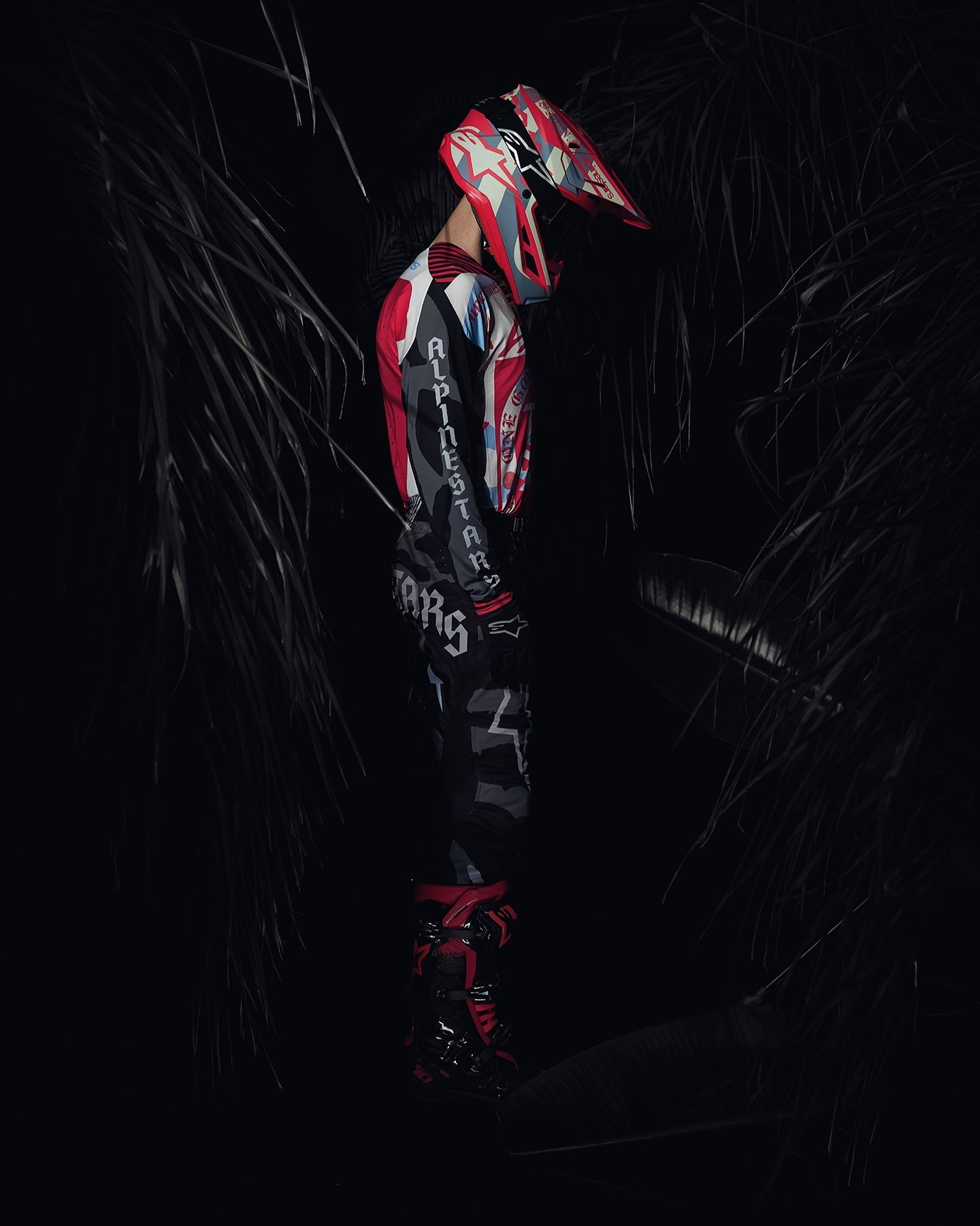 Alpinestars Techstar Beast Coast Motocross Gear Set, black and hot orange racing apparel on rider in jungle setting.