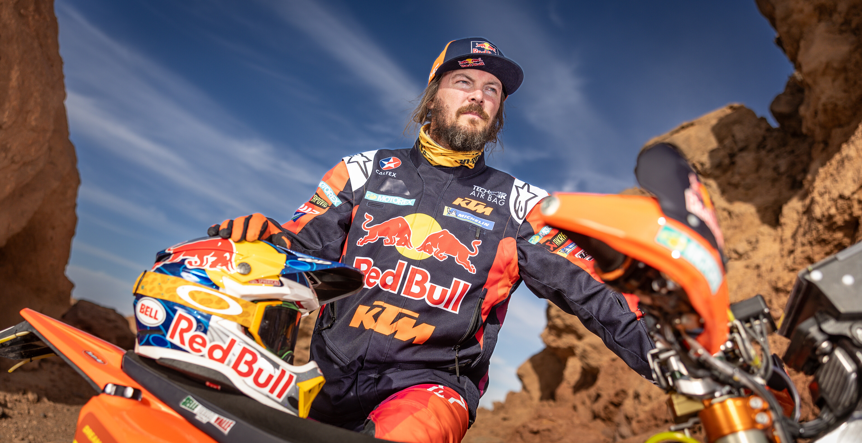 Toby Price wearing a Red Bull KTM enduro jacket by Alpinestars sitting on a motorcycle with a blue sky background
